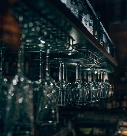 A dimly lit bar interior with rows of hanging wine glasses and bottles in the background.